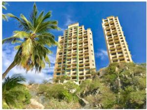 two tall buildings on the beach with palm trees at El Peñón frente al mar in Gaira