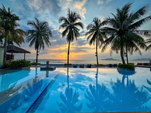 a pool with palm trees and the ocean at sunset at Minitel By The Sea - Pranburi in Sam Roi Yot