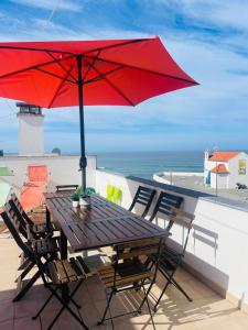 a wooden table with a red umbrella on a balcony at Sunset Beach House in Zambujeira do Mar