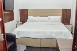 um quarto com uma cama branca com uma cadeira e uma televisão em Kosam Global Hotel and Suites em Uyo