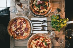 three pizzas on a wooden table with wine glasses at Hyggeligt golfhus i Himmerland in Farsø