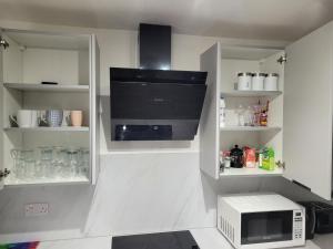 a kitchen with a microwave and a counter with shelves at RentUnique Nimrod House 2 bed ample parking in Crawley