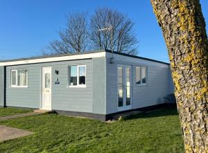 a small grey caravan on a lawn next to a tree at Saltwater Chalet in Kessingland