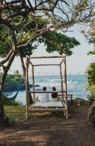2 personnes assises sur une balançoire donnant sur l'océan dans l'établissement Glamping Las Olas by Rotamundos, à Montepio