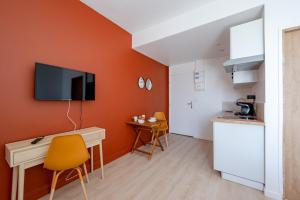 Il comprend une cuisine aux murs orange, un bureau et une télévision. dans l'établissement Les Maisons Acajou - Valenciennes, à Valenciennes