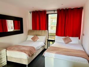 2 camas en una habitación con cortinas rojas en London Regent Studio Apartments, en Londres