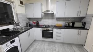 a kitchen with white cabinets and a sink and a stove at Garland Modern Close To Station 3 Bedroom City Apartment in London