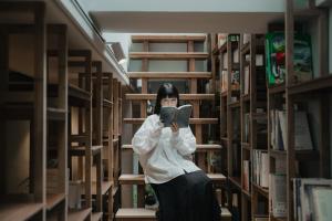 a woman standing in a library reading a book at Norden Ruder Hostel Taitung Branch 2 in Taitung City