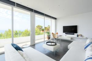 Una sala de estar con muebles blancos y grandes ventanales. en Villa Nineten, en Roca Llisa