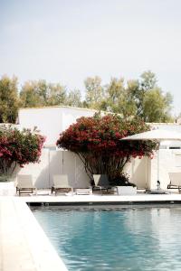 una piscina con sillas, flores y sombrilla en Mas de la Fouque - Hôtel & Spa en Saintes-Maries-de-la-Mer