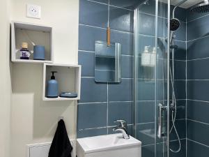 een blauwe betegelde badkamer met een wastafel en een douche bij Maison Jaune in Stains