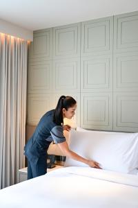 Una mujer está haciendo una cama en una habitación. en Courtyard by Marriott Bangkok Sukhumvit 20, en Bangkok