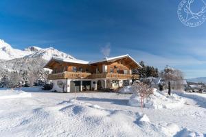 ein großes Holzhaus im Schnee mit Bergen in der Unterkunft Appartements Lärchmoos in Ramsau am Dachstein
