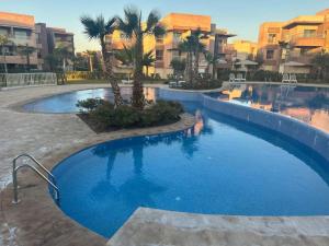 une grande piscine avec des palmiers et des bâtiments dans l'établissement Appartement 3 chambres en rez-de-jardin avec piscine Prestigia Marrakech, à Marrakech