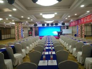 a banquet hall with white tables and chairs and a screen at Xana Hotelle Yining Airport Road Jinwuyuan in Kipekyüzi