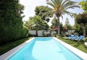 a swimming pool with two blue chairs and palm trees at Beautiful Villa La Caracola in Marbella