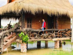 un hombre sentado en un puente de madera delante de una cabaña en Meta Homestay, en Phumĭ Puŏk Chăs