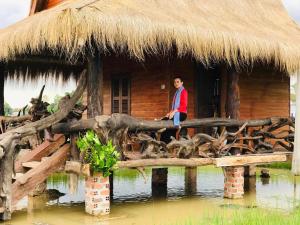 a man sitting on a wooden bridge in front of a hut at Meta Homestay in Phumĭ Puŏk Chăs
