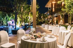 uma mesa com comida com mesas e cadeiras brancas em Riverton Hotel em Samut Songkhram