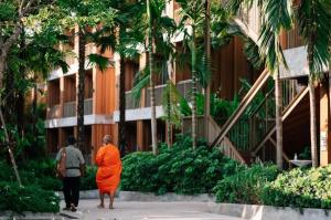 dos personas vestidas de naranja caminando frente a un edificio en Riverton Hotel en Samut Songkhram