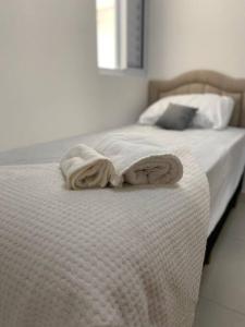 a bed with white sheets and two towels on it at Apartamento próximo a uopeccan in Umuarama