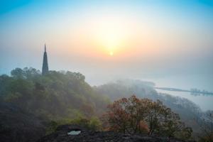 a misty sunrise with a clock tower on a hill at Hi Inn Hangzhou Sijiqing Qiutao North Road in Hangzhou