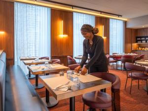 a woman standing at a table in a restaurant at Novotel SPA Rennes Centre Gare in Rennes