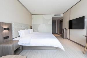 a bedroom with a large white bed and a flat screen tv at Hanting Hotel Zhengzhou South Longhu Shawoli Metro Station in Guodian