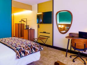 a bedroom with a bed and a desk and a mirror at Novotel Avignon Nord in Sorgues