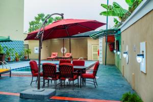 Crownsville Hotel - Airport Road في بورت هاركورت: طاولة وكراسي مع مظلة حمراء على الفناء