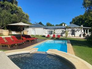 a swimming pool with red chairs and a house at Banhoek Corner Guesthouse in Stellenbosch