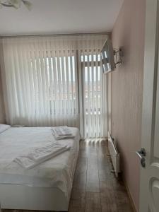 a bedroom with a bed and a large window at Апартамент Градски Парк in Dobrich