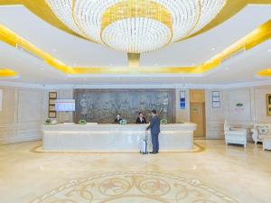 un hombre de pie en un vestíbulo con una gran lámpara de araña en Vienna Hotel Hubei Xiangyang Tang City Gulou en Xiangyang