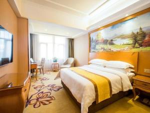 ein Schlafzimmer mit einem großen Bett und einem Gemälde an der Wand in der Unterkunft Vienna Hotel Qinghai Xining Deling Halu City East Wanda Plaza in Xining