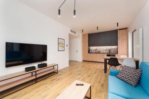 a living room with a blue couch and a large tv at Apartament na Sosnowej Wydmie - Osiedle Shellter in Rogowo