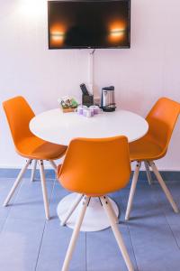 tavolo bianco con sedie arancioni e TV a parete di LOGIS Hôtel & Restaurant Le Soleil D'or a Montigny-la-Resle