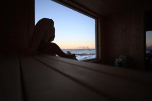 una persona sentada en el alféizar de una ventana mirando hacia el océano en Vannøy Sport og Havfiske en Vannvåg