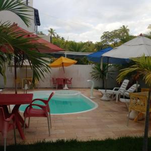 una piscina con ombrelloni, sedie e tavolo di Residencial e Pousada Sea La Vie a Maragogi