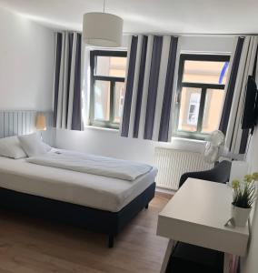 a bedroom with a bed and a desk and two windows at Hotel Café Rhönperle in Bad Neustadt an der Saale