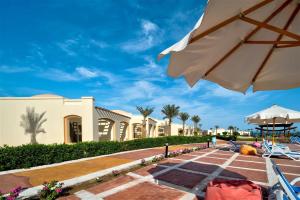 a patio with an umbrella and chairs and a building at Amarina Queen Resort Marsa Alam in Marsa Alam City