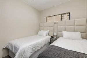 a white bedroom with two beds and a window at Waterfall Ridge - Retreat in the heart of Midrand in Midrand
