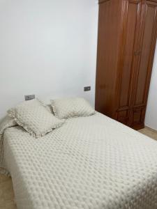 a white bed with two pillows and a wooden cabinet at la laja 38 in Las Palmas de Gran Canaria