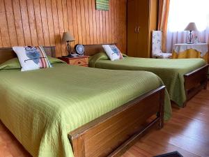 two green beds in a room with wooden walls at Hotel Cabañas Caribe in Los Vilos