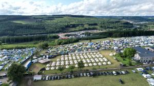 an aerial view of a parking lot with tents at GrandPrixCamp closest to the track including track view in Stavelot