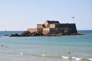people swimming in the ocean with a castle in the background at Hôtel de la Cité in Saint Malo