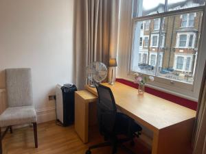 einen Schreibtisch mit einem Ventilator, einem Stuhl und einem Fenster in der Unterkunft 15 min to The Heart of London - Charming 2 bed Apartment in London