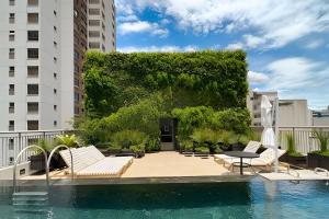 una piscina con tumbonas y una pared verde en Zainalofts7 Moema - 1km Ibira e 200m metrô 509 ID, en São Paulo