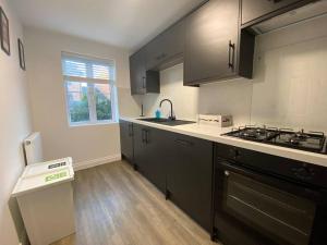 a kitchen with black cabinets and a sink and a stove at Stylish 3-Bed House with Free Parking & Netflix by HP Accommodation in Northampton