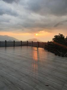 a sunset over a patio with a fence and mountains at Serenity Valley Ambuluwawa Resort in Kandy