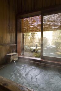 a bath tub with water in a room with a window at Ekinariya Ryokan in Kusatsu